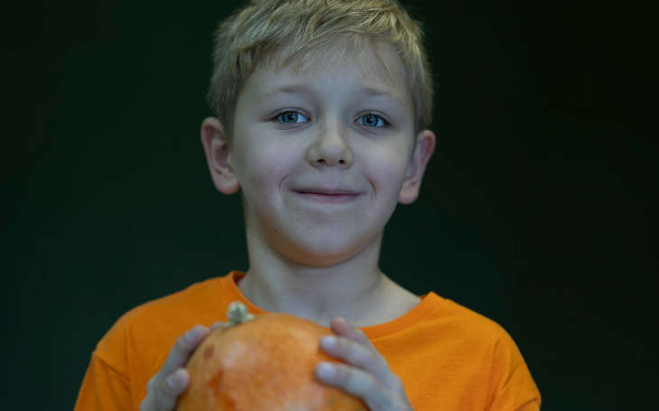Chłopiec trzymający dynię, uśmiechający się do kamery.