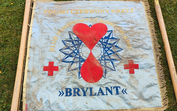 Flaga Polskiego Czerwonego Krzyża z logo klubu krwiodawców.
