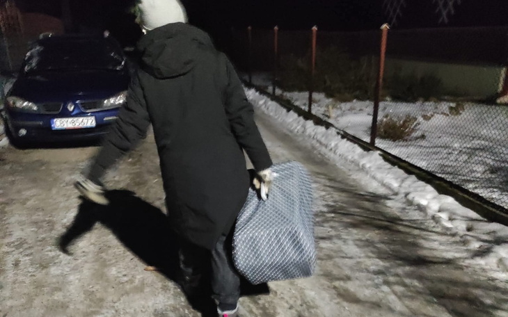 Osoba w czarnym płaszczu idąca nocą z torbą.