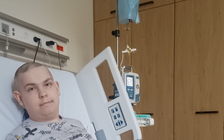Chory chłopak leży na łóżku w szpitalu, za inhalator i sprzęt medyczny w tle.