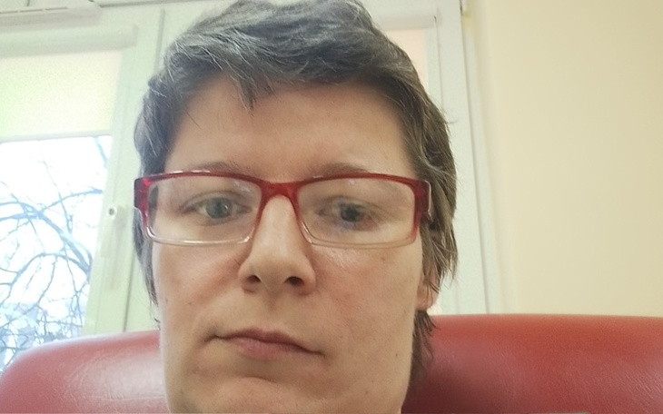 Portret kobiety w okularach, siedzącej na czerwonym fotelu.