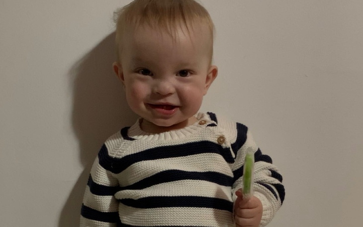 Uśmiechnięty niemowlak w sweterku, trzymający lizaka.