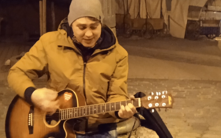 Mężczyzna grający na gitarze w zimowej scenerii.