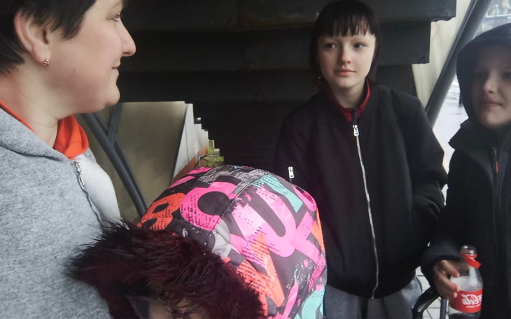 Grupa dzieci i dorosłych w deszczowy dzień, schronieni pod schodami.