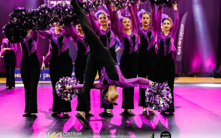 Grupa cheerleaderek w kolorowych strojach na scenie.
