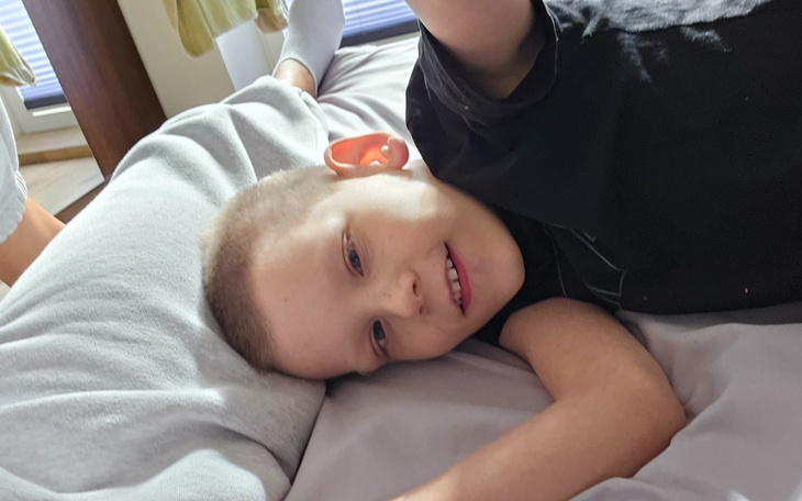 Chłopiec leży na poduszce, uśmiechając się do kamery.