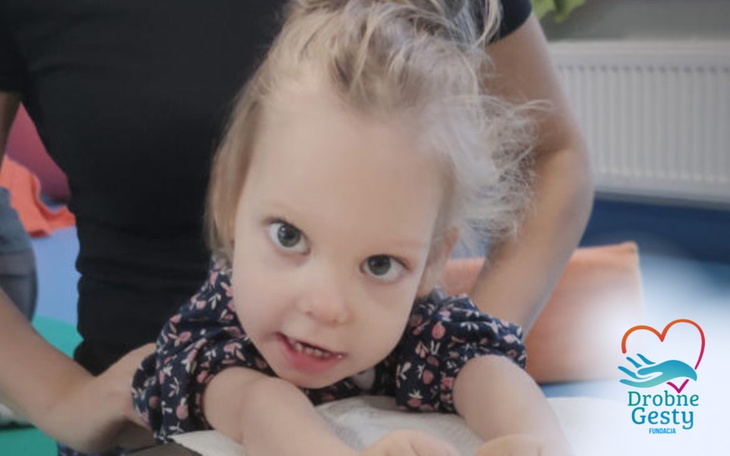 Mała dziewczynka uśmiechająca się podczas zajęć terapeutycznych.