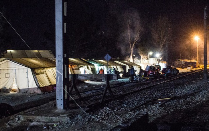 Obozowisko z namiotami przy torach kolejowych w nocy.