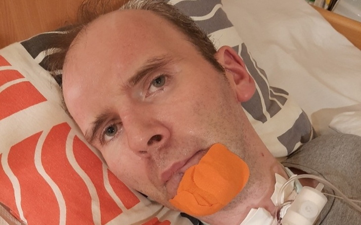 Mężczyzna leżący w łóżku, z opatrunkiem na twarzy.