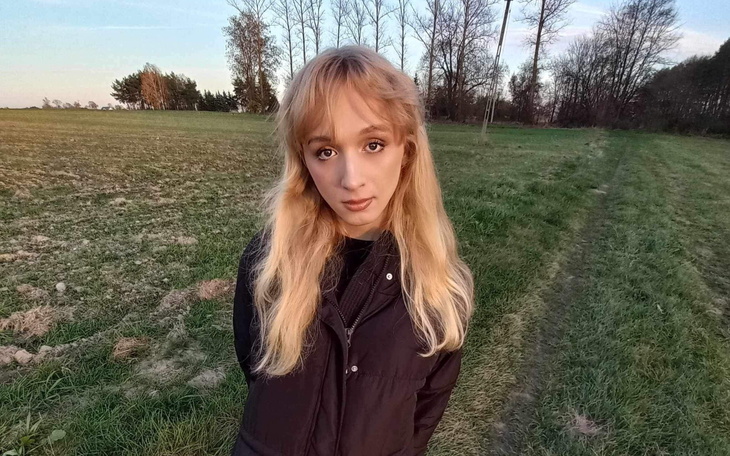 Młoda kobieta na tle zielonego krajobrazu, patrzy w obiektyw.