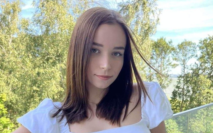 Młoda kobieta w białej bluzce, uśmiechająca się na tle natury.