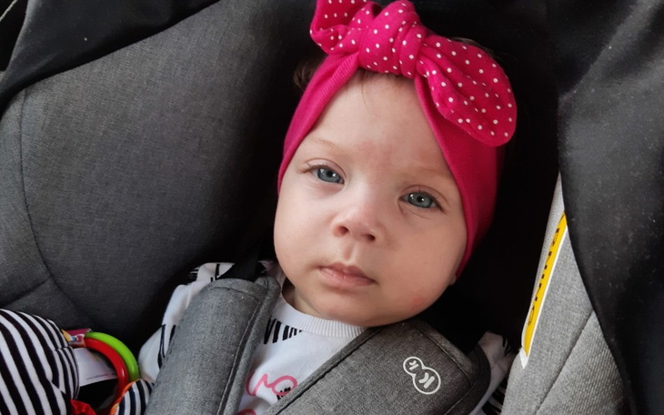 Mała dziewczynka w foteliku samochodowym z różową opaską.