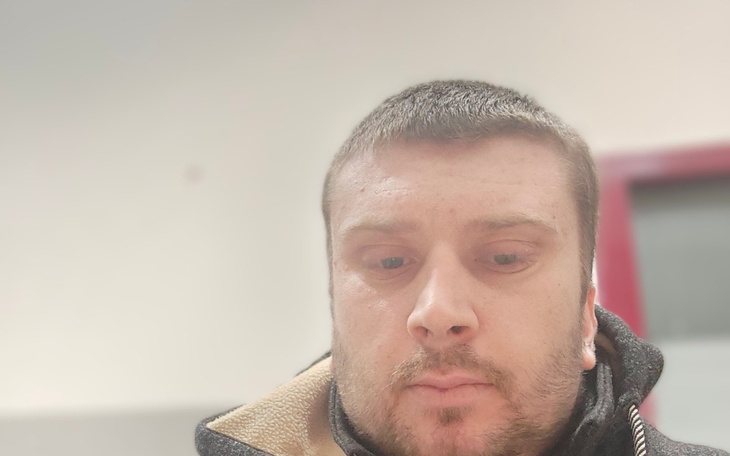Mężczyzna w szarej kurtce, patrzący w dół.