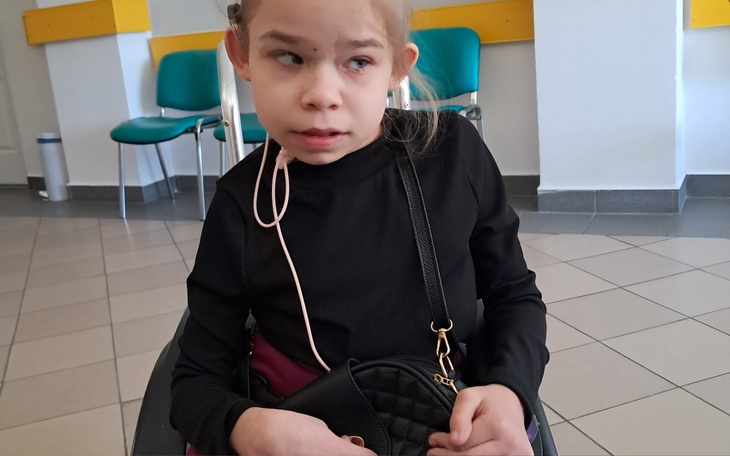 Dziewczynka w czarnym swetrze, siedząca na wózku inwalidzkim.