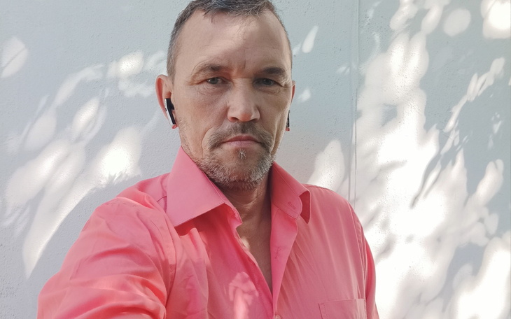 Mężczyzna w różowej koszuli pozujący do zdjęcia.