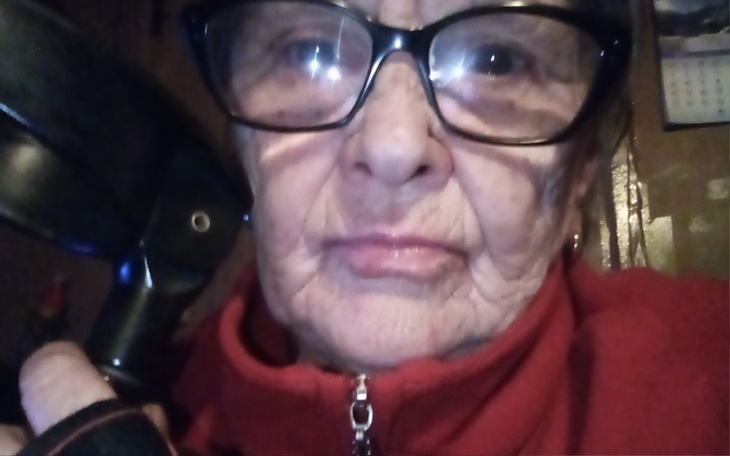 Starsza kobieta w okularach, trzymająca przedmiot w ręku.