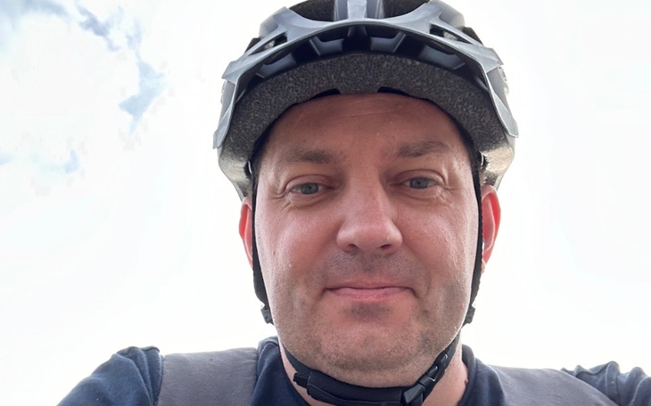 Mężczyzna w kasku rowerowym, uśmiechający się do kamery.