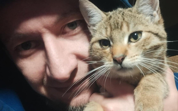 Mężczyzna trzymający kota, obaj uśmiechnięci do kamery.