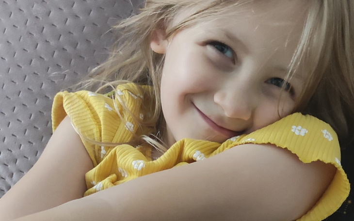 Uśmiechnięta dziewczynka w żółtej sukience, przytulająca się.