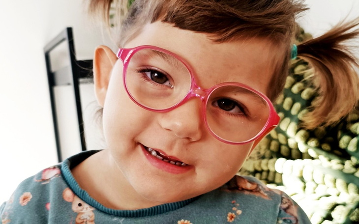Mała dziewczynka z okularami, uśmiechająca się do kamery.