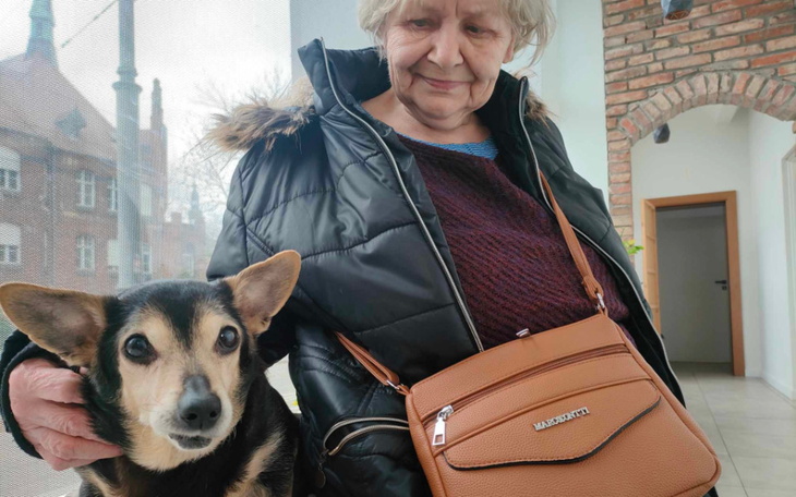 Starsza kobieta z psem, uśmiechają się w jasnym pomieszczeniu.