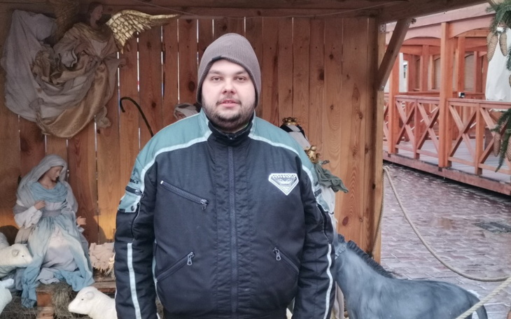 Mężczyzna w kurtce, stojący w drewnianej chatce.