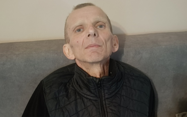 Mężczyzna z chudą sylwetką, siedzący na kanapie.