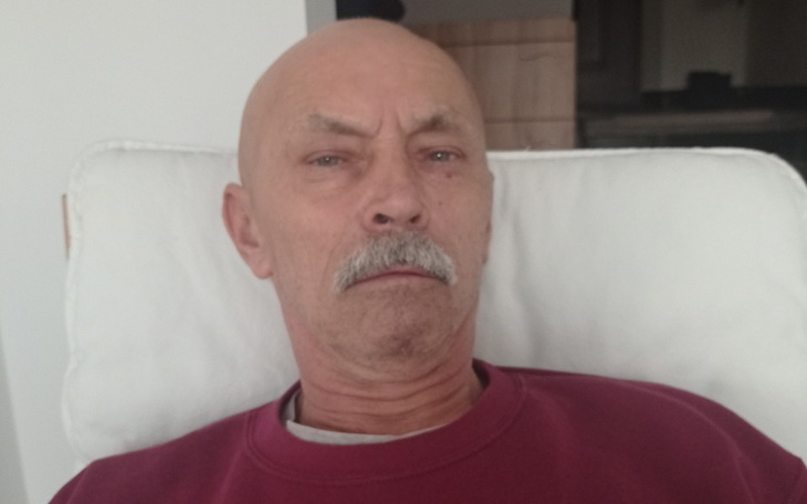 Mężczyzna z poważnym wyrazem twarzy siedzący na kanapie.