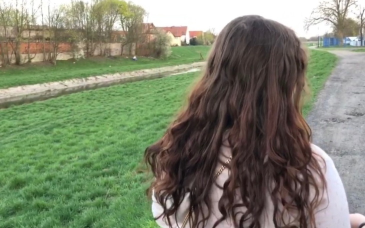 Dziewczyna z długimi, kręconymi włosami spacerująca wzdłuż rzeki.