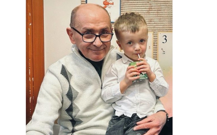 Dziadek z wnuczkiem siedzą na krześle, obaj uśmiechnięci.