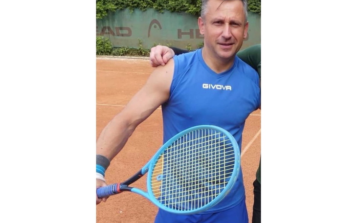 Mężczyzna w niebieskiej koszulce trzyma rakietę tenisową na korcie.