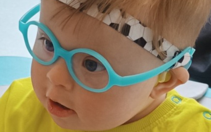 Mały chłopiec w okularach i opasce na głowie, uśmiechający się.