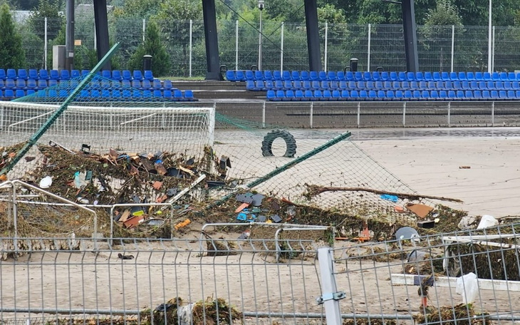Zniszczone boisko piłkarskie z porozrzucanymi śmieciami i zniszczoną siatką.