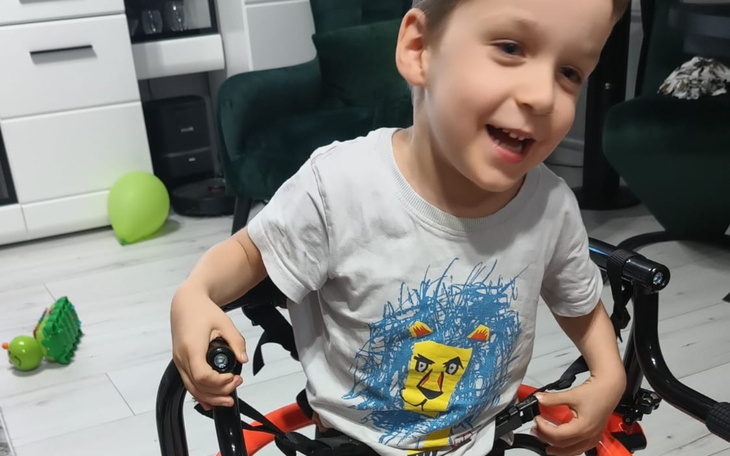 Chłopiec w wózku, uśmiechający się i bawiący się zabawkami.