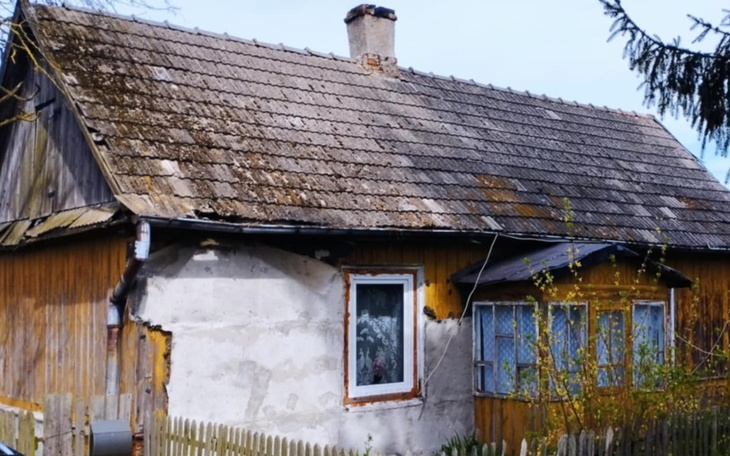 Zniszczony dom z drewnianą elewacją i uszkodzonym dachem.
