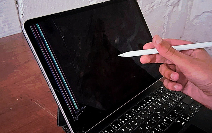 Ręka trzymająca rysik nad uszkodzonym ekranem laptopa.