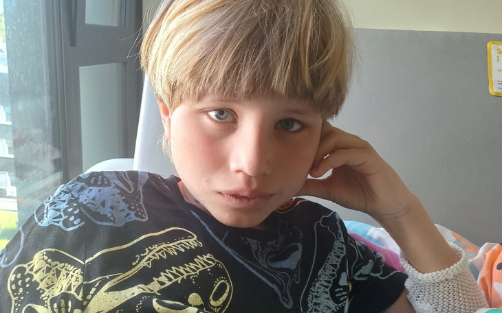 Chłopiec z krótkimi włosami, siedzący na łóżku z zamyśloną miną.