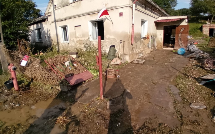 Widok na zniszczony dom po powodzi, z bałaganem na podwórku.