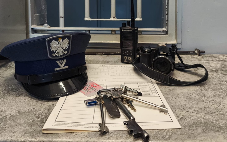 Zestaw policyjny z dokumentami, kluczami i aparatem na stole.