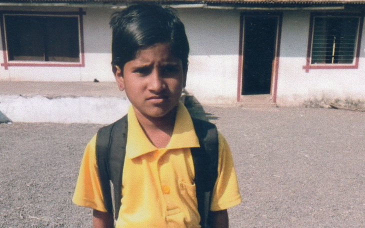 Chłopiec w żółtej koszuli, stojący przed budynkiem.