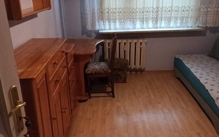 Pusty pokój z drewnianymi meblami i oknem z firanką.