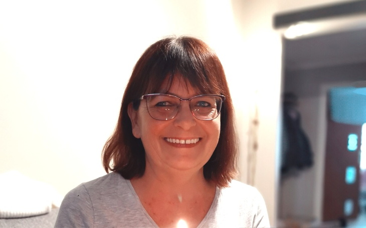 Uśmiechnięta kobieta w okularach, siedząca w jasnym pomieszczeniu.