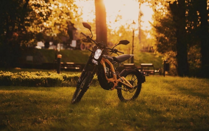 Motocykl w promieniach zachodzącego słońca, otoczony zielenią.