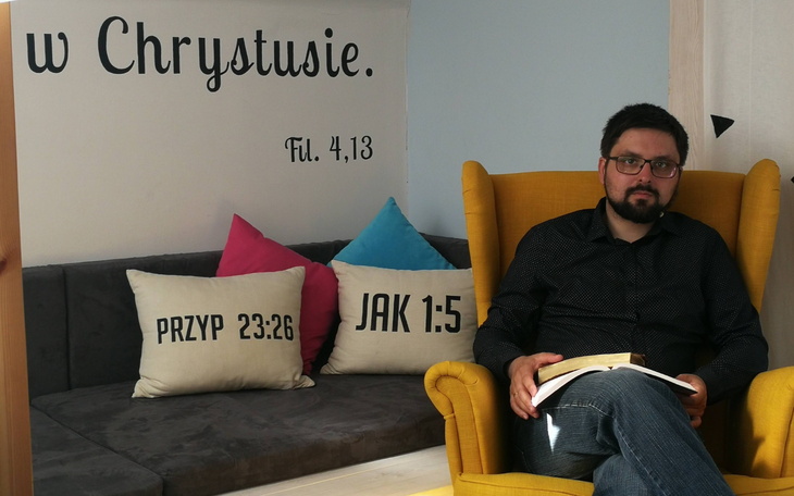 Mężczyzna siedzący w żółtym fotelu, czytający książkę.