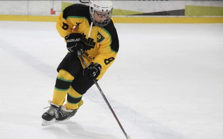 Młody hokeista w akcji na lodowisku, w żółtej koszulce.