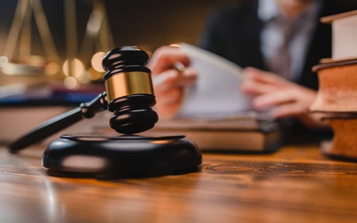 Młot sędziowski na stole, w tle osoba przeglądająca dokumenty.