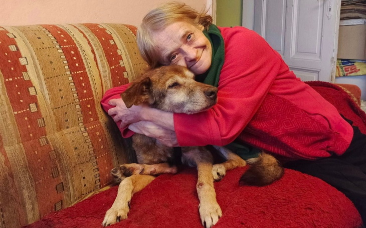 Starsza kobieta przytulająca psa na kanapie.