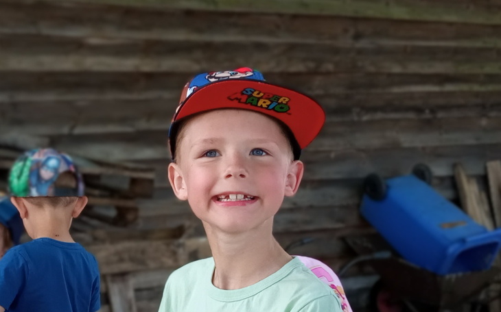 Chłopiec w czapce Super Mario, uśmiechnięty na tle drewnianej ściany.