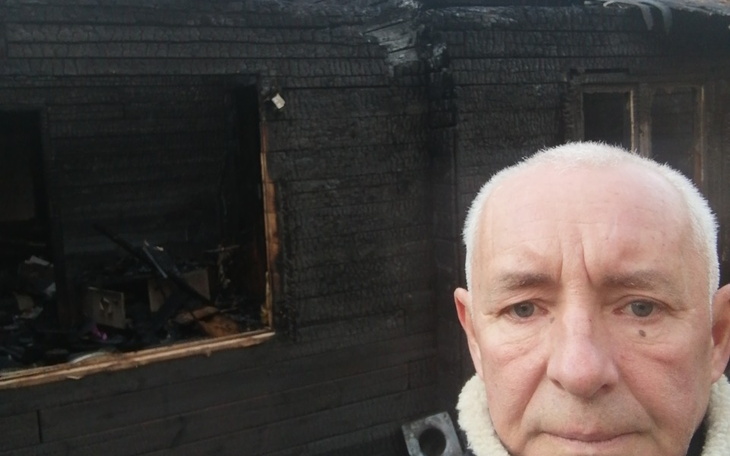 Mężczyzna stoi przed zniszczonym budynkiem po pożarze.