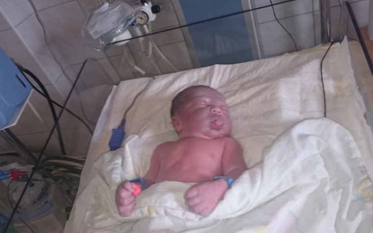 Noworodek w inkubatorze, otoczony sprzętem medycznym.